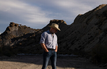 Fototapeta premium Adult man in cowboy hat standing against mountains in Tabernas desert. Almeria, Spain