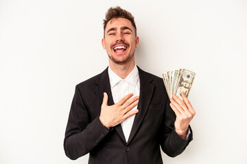 Young caucasian business man holding bank notes isolated on white background laughs out loudly keeping hand on chest.
