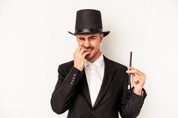 Young caucasian wizard man holding a wand isolated on white background biting fingernails, nervous...