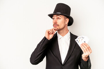 Young caucasian wizard man holding a magic cards isolated on white background looking sideways with doubtful and skeptical expression.