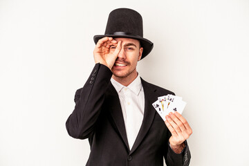 Young caucasian wizard man holding a magic cards isolated on white background excited keeping ok...