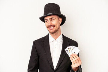 Young caucasian wizard man holding a magic cards isolated on white background looks aside smiling,...