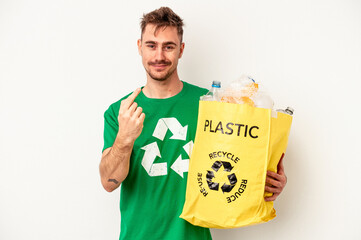 Young caucasian man recycled plastic isolated on white background pointing with finger at you as if...