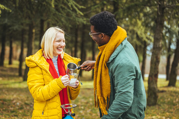 Fototapeta premium A happy and in love couple is sitting on the mountain, talking and drinking coffee together in the fall. The smiling couple relaxes and enjoys camping outdoors on vacation.
