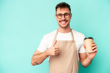 Young store clerk man holding a coffee isolated on blue background smiling and raising thumb up
