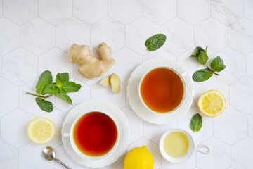 Two cups of tea, lemon, mint leaves, ginger, honey on the white marble background. Layout. Heath. Composition. Place for text.