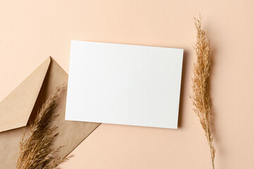 Greeting card mockup with envelope and dry plant decorations on beige background