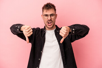 Young caucasian man isolated on pink background showing thumb down and expressing dislike.