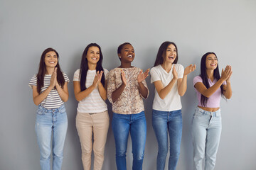 Happy multiethnic female audience giving round of applause. Group of positive smiling young women applauding speaker. Studio portrait of five cheerful beautiful ladies standing by wall clapping hands