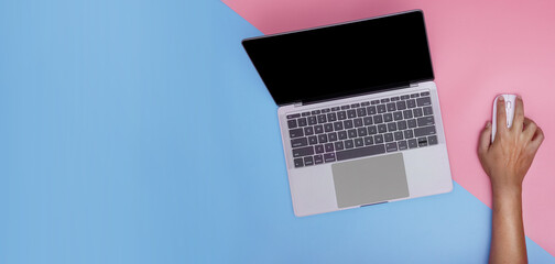 Person using a laptop computer from above on pink and blue background. free text copy space.
