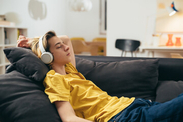 teenage boy relaxing on sofa and listening to a music