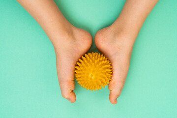 green needle ball for massage and physical therapy on a green background with a child's foot, the concept of prevention and treatment of foot valgus