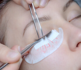 A young woman undergoes an eyelash extension procedure in a beauty salon. Top view, close, selective focus