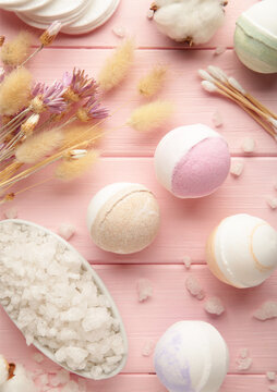 Aroma bath bombs in spa composition with dry flowers and salt on pink background. Vertical photo.