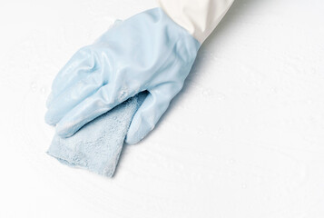 Female hand in rubber glove wipes surface with rag, white background.