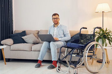 Fototapeta na wymiar With laptop on the legs. Disabled man in wheelchair is at home