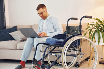Sitting on sofa with laptop on legs. Disabled man in wheelchair is at home