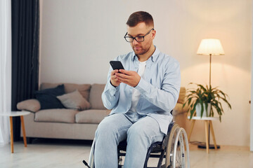 Using phone. Disabled man in wheelchair is at home
