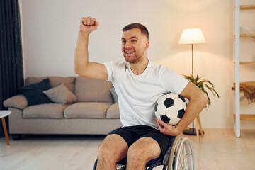 With soccer ball. Disabled man in wheelchair is at home