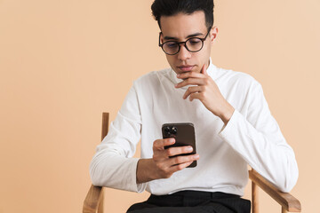 Young middle eastern man using cellphone while sitting on chair