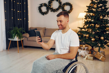 Using smartphone to communicate with people. New year is coming. Disabled man in wheelchair is at home