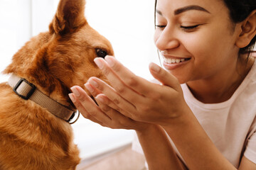 Young hispanic woman laughing while petting her dog