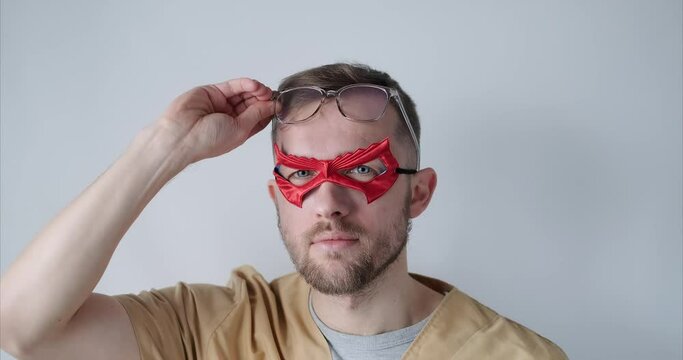 Portrait of male superman doctor or nurse. Portrait of a handsome caucasian male doctor wearing red face superhero mask, eyeglasses and beige medical uniform. High quality 4k video footage