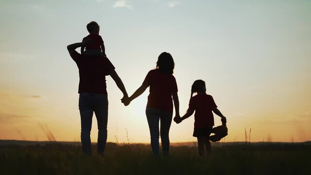Happy family concept. People walk on grass in field. Girl with teddy bear in her hands.Group of people walk at sunset in park.Active lifestyle concept.Family in natural park.Parents with child in park