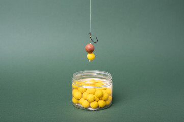 Carp fishing tackle concept, sharp fishing hook with boilie for carp fish. Yellow boilie on green backdrop.