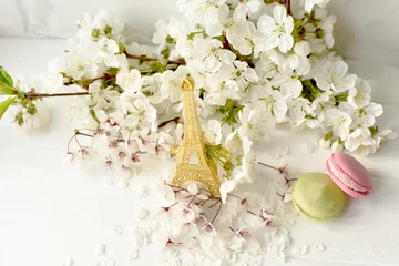 Zelfklevend Fotobehang Eiffel tower figurine, macarons and branches with white cherry blossoms on a white background. Spring still life, travel France. © Ann Stryzhekin
