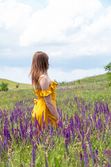 Adult girl stands with her back in the middle of sage blossom in meadow. Communication with nature. Selective focus.