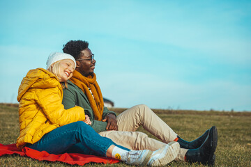 Young beautiful couple blonde girl in warm clothes and man in white t-shirt having fun in the grass in a field in nature at sunset. Happy young loving couple sitting, laughing and hugging