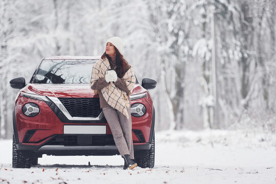 In front of her car. Beautiful young woman is outdoors near her red automobile at winter time