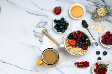 Healthy breakfast or snack, with cup of coffee, oat with berry, honey and ripe sweet berries on white marble table. top wave, flat lay.