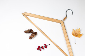 Empty wooden clothes hanger, fir cone and dry leaf on white background. Autumn sales and discounts concept, flat lay with copy space.