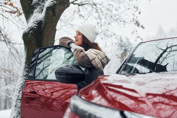 Walking out off car. Beautiful young woman is outdoors near her red automobile at winter time
