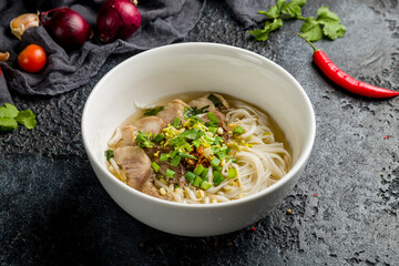 Soup Pho Bo with beef and noodles on white bowl on dark stone table