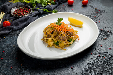 fried Udon with beef and vegetables on white plate on dark stone table, Chinese cuisine