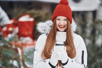 Obraz premium With cup of drink in hands. Happy young woman standing outdoors and celebrating christmas holidays
