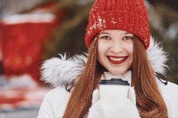 With cup of drink in hands. Happy young woman standing outdoors and celebrating christmas holidays