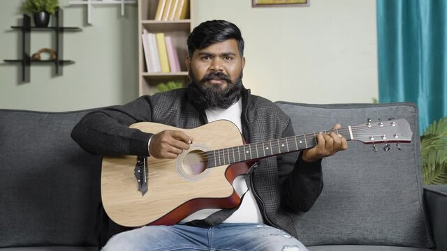 Young beard man teaching about guitar by looking at camera from home - concept of online or virtual music class, hobbies and professional artist.