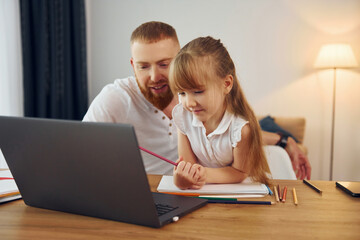 Using laptop. Father with his little daughter is at home together