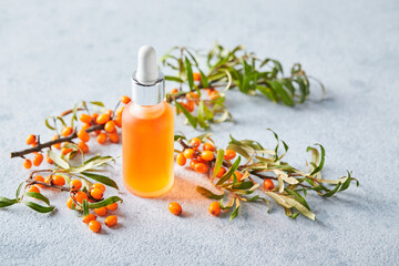 Glass bottle with sea buckthorn oil, berries and branches of sea buckthorn on light background