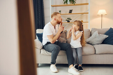 On the sofa. Having fun. Father with his little daughter is at home together