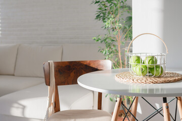 light Scandinavian interior. Green apples in a basket on a white table. Stylish modern interior in the sunlight