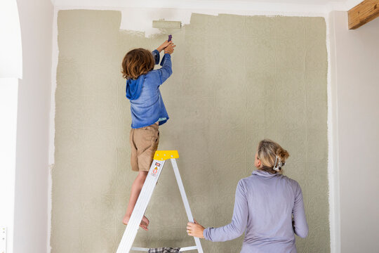 A woman and an eight year old boy decorating a room, painting walls. 