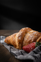 breakfast croissant with powdered sugar and strawberry dark background with black and white napkin