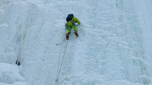 Alpinist man with ice tools axe climbing a frozen waterfall, a large wall of ice