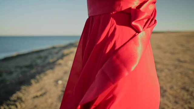 Close-up of red dress fabric on Caucasian attractive woman ripples in the wind. Walk on the sea in windy weather