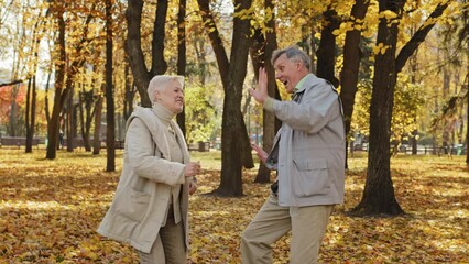 Positive elderly family couple dancing in autumn park smiling happy pensioners have fun outdoors carefree old man and woman celebrate special event spend time together healthy active lifestyle concept